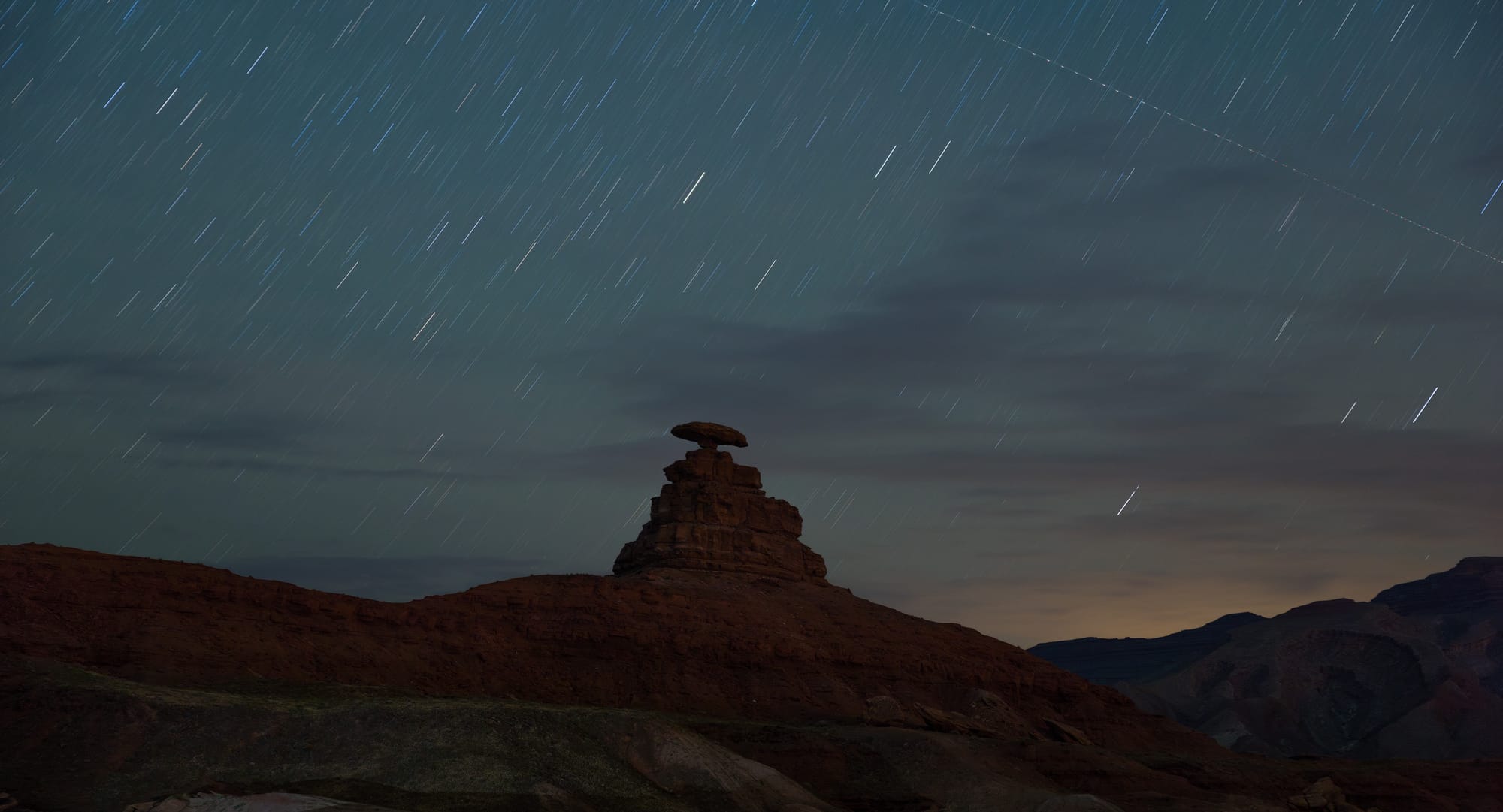 A long exposure night photo with star trails of the Mexican Hat formation in Monument Valley